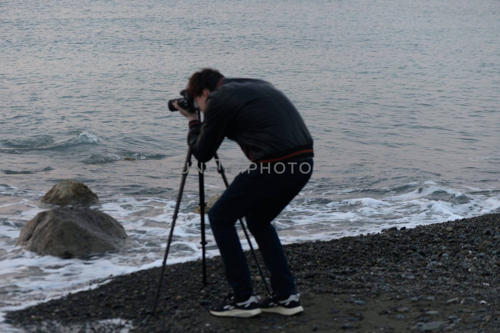A photographer focuses intently on the waves, creating art at twilight by the serene beach.