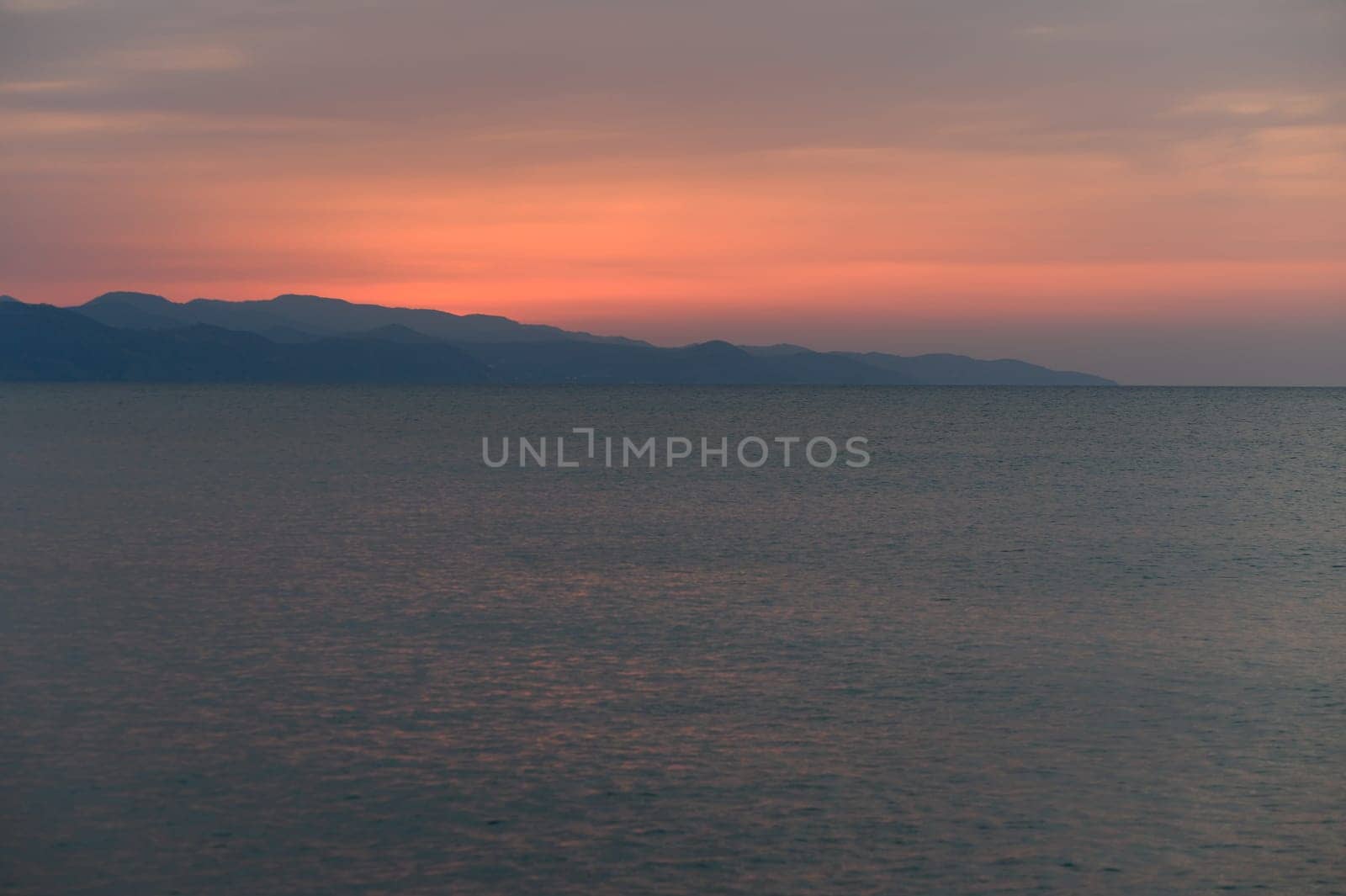 Gentle waves reflect the stunning hues of sunset as mountains silhouette against the colorful evening sky.
