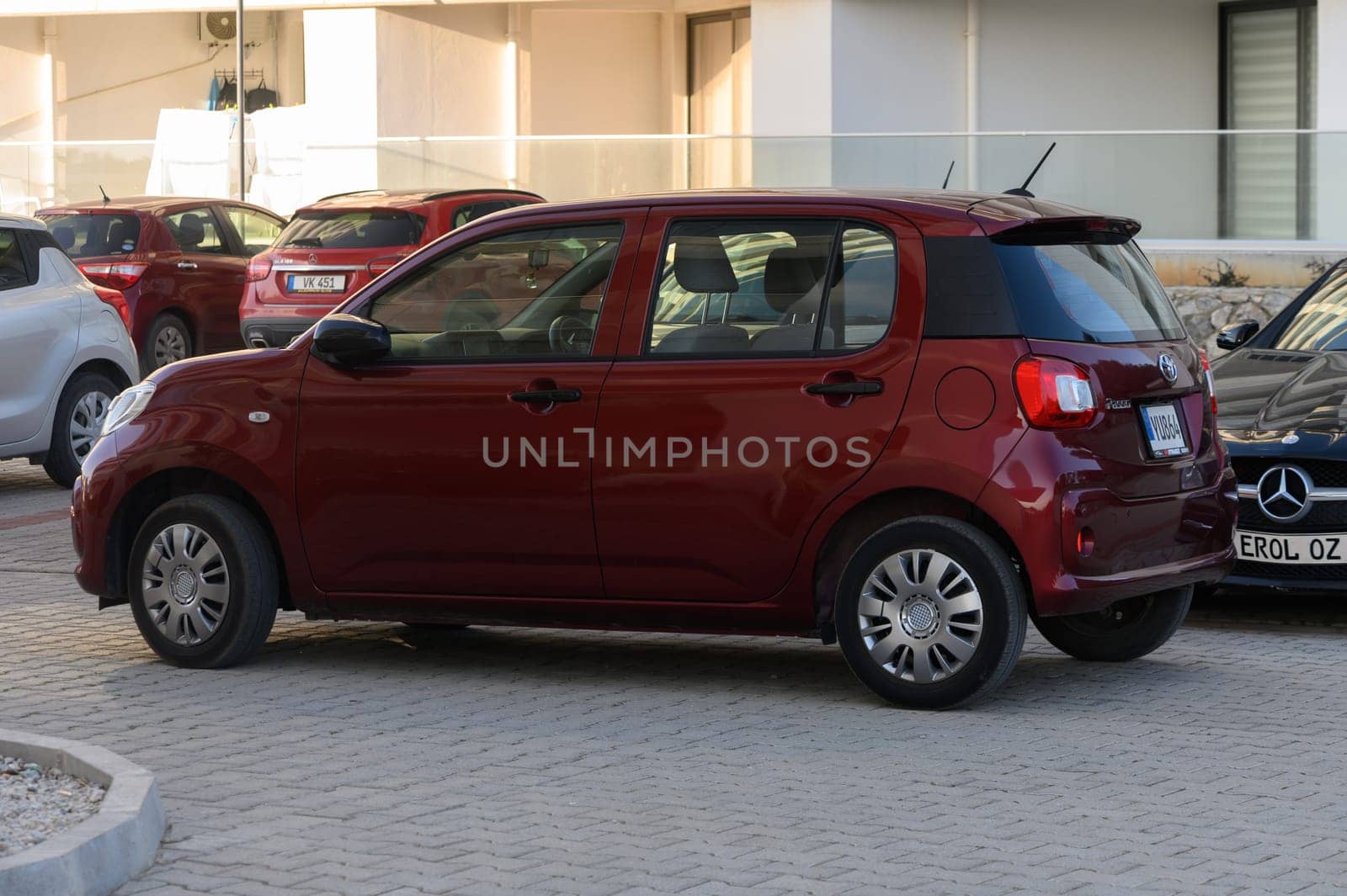 A cheerful red compact car is parked snugly among other vehicles in a vibrant parking lot filled with sunlight.