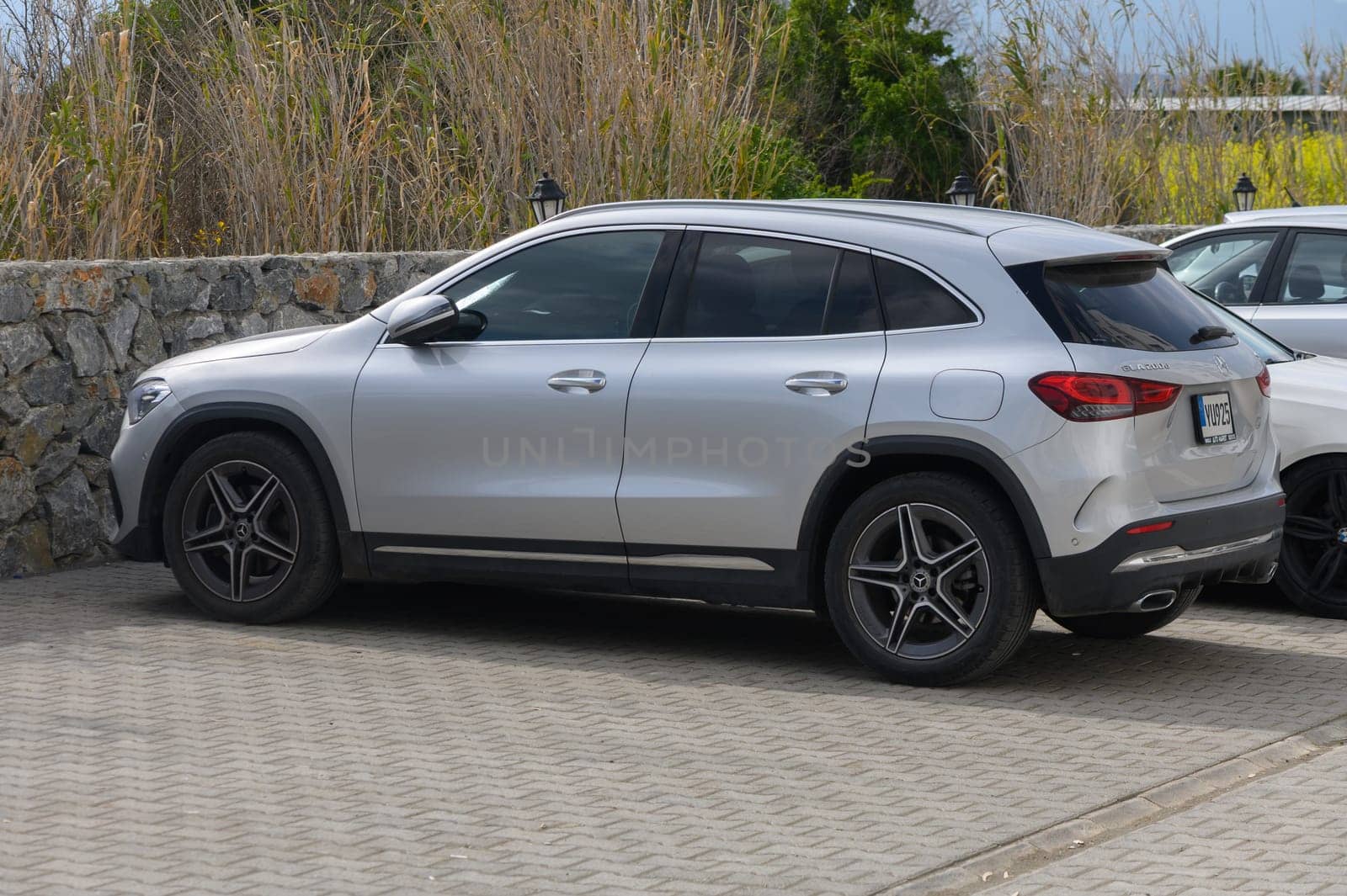 A sleek silver SUV is parked next to a textured stone wall in a beautiful coastal setting, enjoying the sunny day.