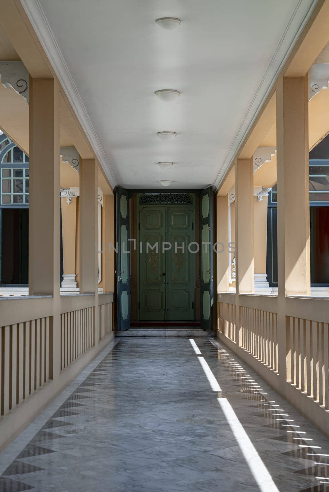 Bangkok, Thailand - Mar 02, 2025 - Perspective view of Long corridor with lantern ceiling and columns leading into entrance green ancient door at Khun Phrom Palace or Bank of Thailand Museum. use it as your Wallpaper, Poster and Space for text, Selective focus.