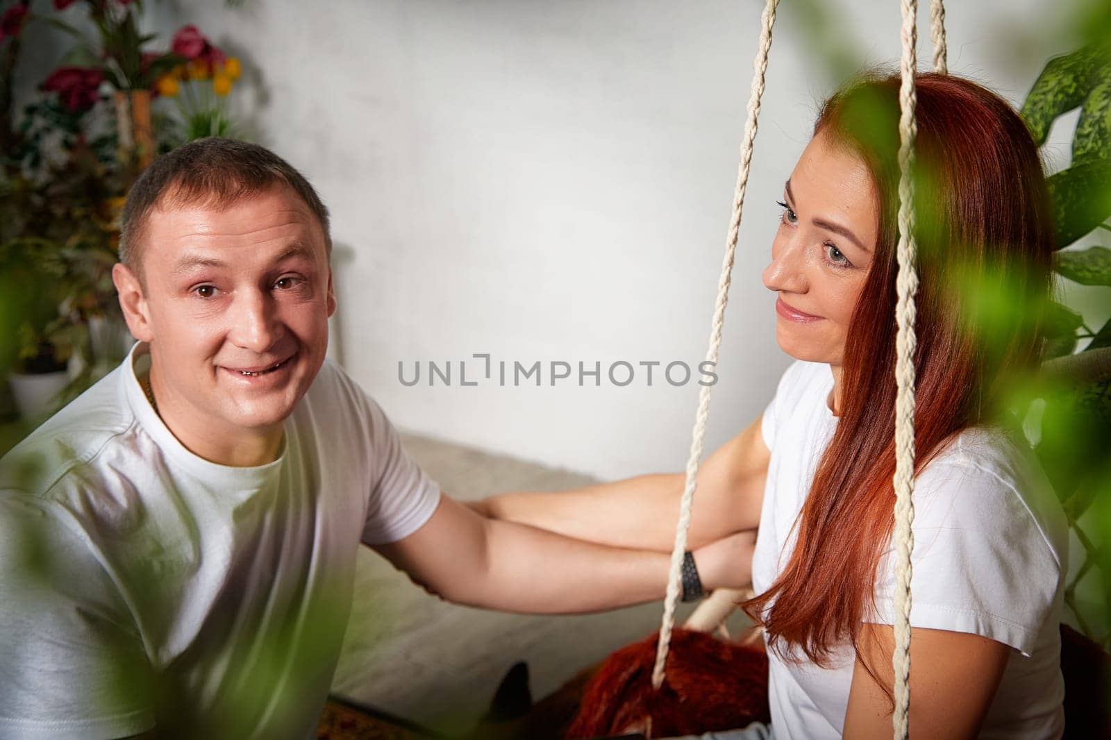 A mature couple enjoys a tender moment together in a warm, inviting space filled with plants and natural light.