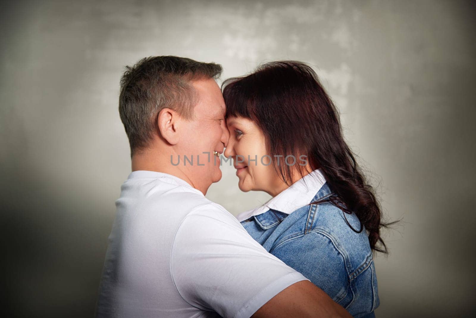 A middle-aged couple shares a joyful moment, embracing and smiling at each other inside their apartment, showcasing their love and connection.