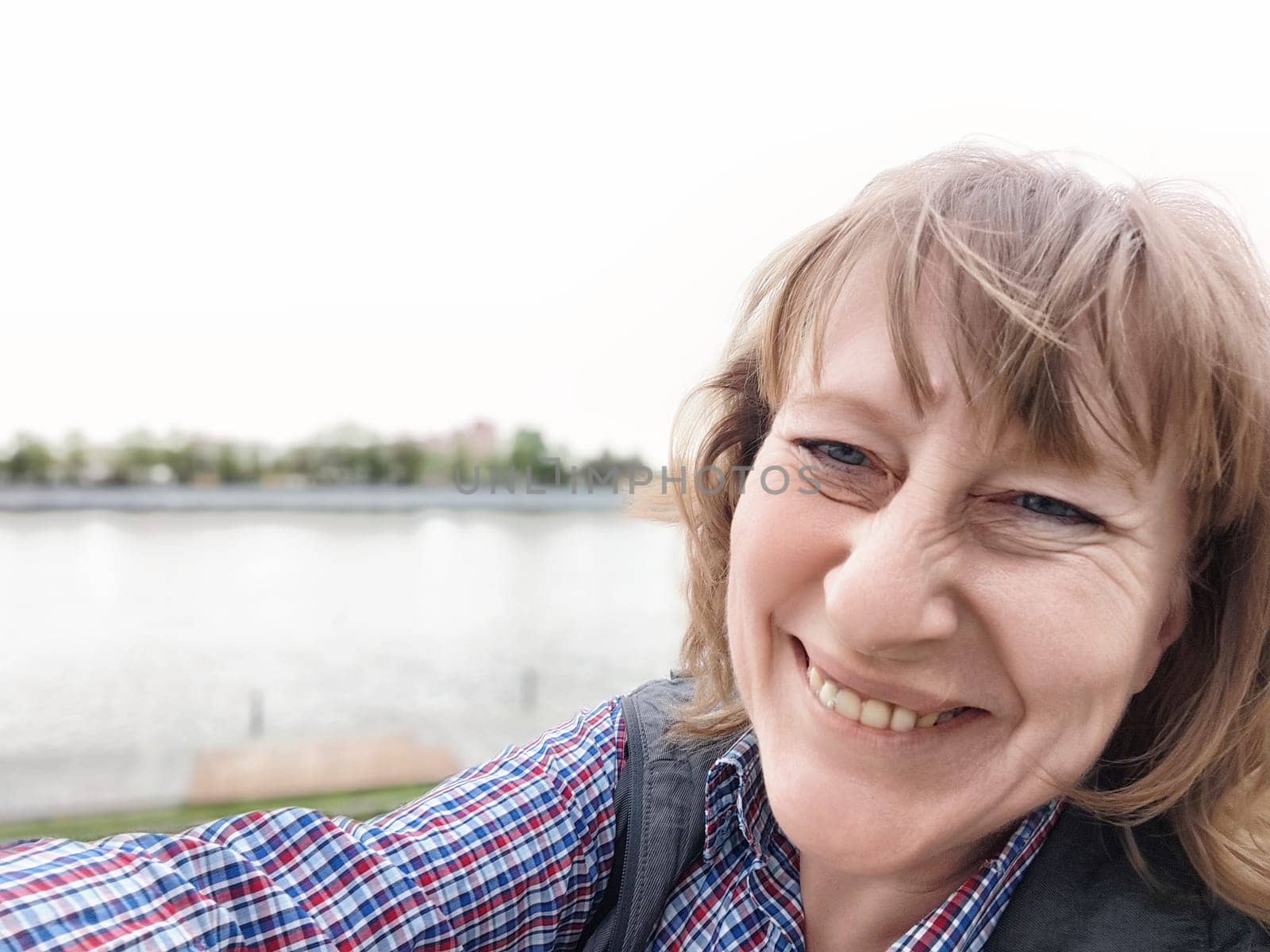 A middle-aged female traveler captures a joyful selfie near the water while exploring a beautiful destination.