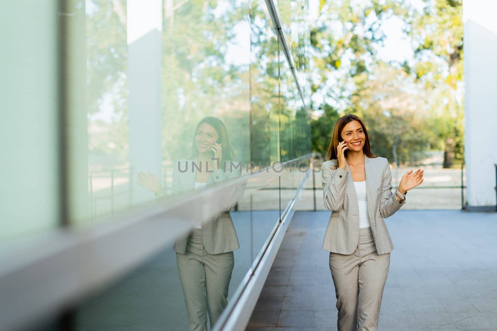 Professional woman walks with ease, smiling as she focuses on her phone, blending modern lifestyle with the tranquility of nature in the background