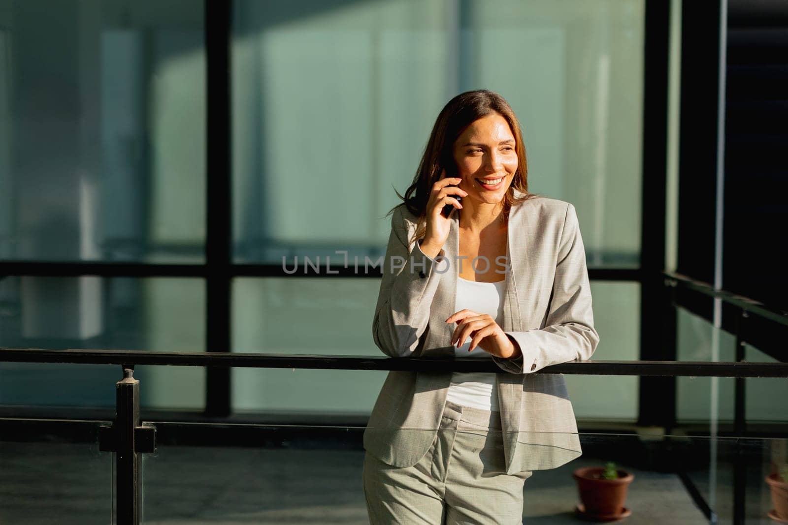 In a bright, contemporary office, a businesswoman engages with her smartphone, showcasing a blend of professionalism and warmth as sunlight filters through the glass