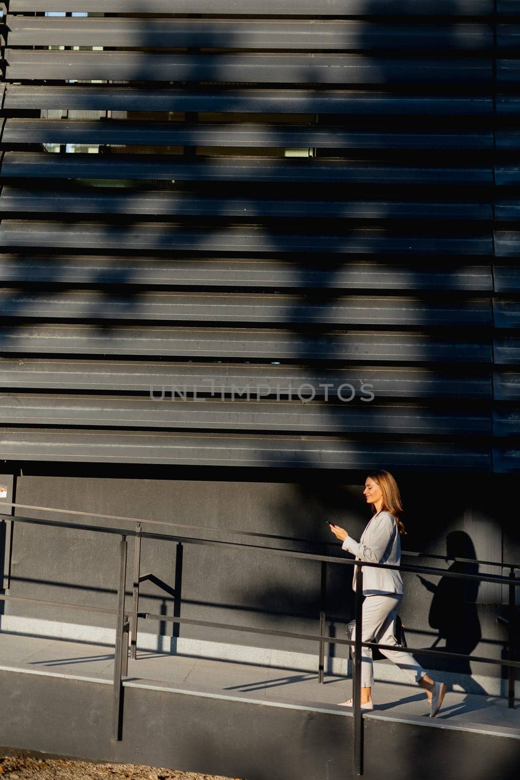 Young business woman strolls through a contemporary outdoor space, exuding confidence while dressed in sleek attire. The warm light accentuates her stylish presence