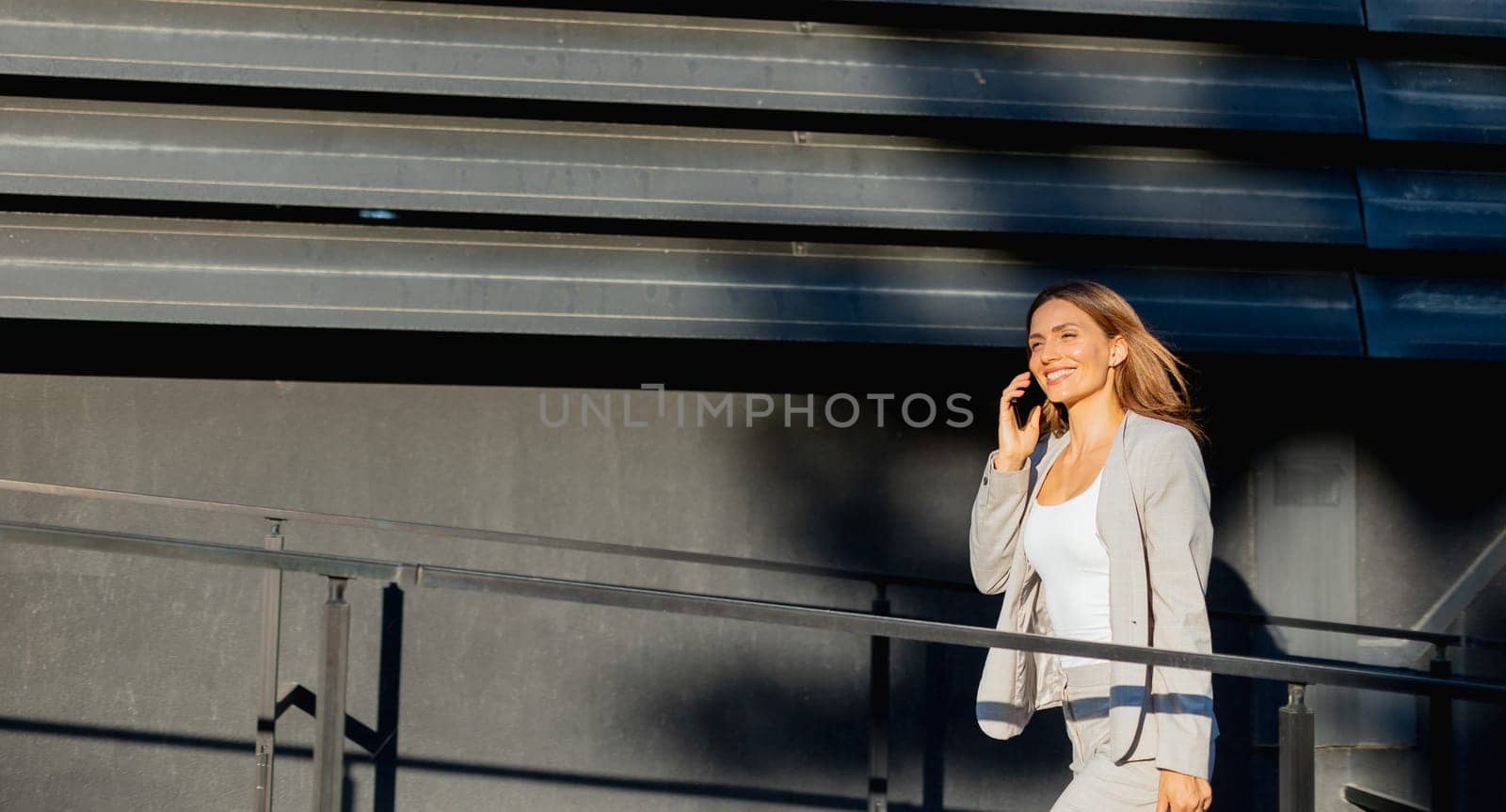 Young business woman strolls through a contemporary outdoor space, exuding confidence while dressed in sleek attire. The warm light accentuates her stylish presence