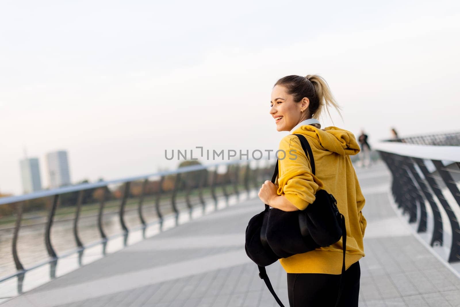A carefree woman walks along a contemporary riverside path, her cheerful demeanor captured as she enjoys the picturesque sunset and fresh air.