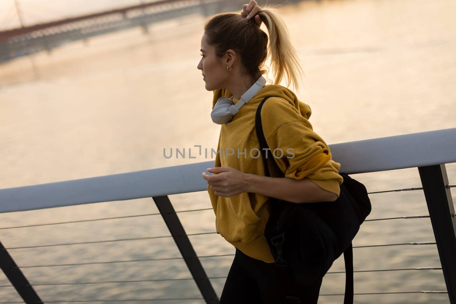 A carefree woman walks along a contemporary riverside path, her cheerful demeanor captured as she enjoys the picturesque sunset and fresh air.