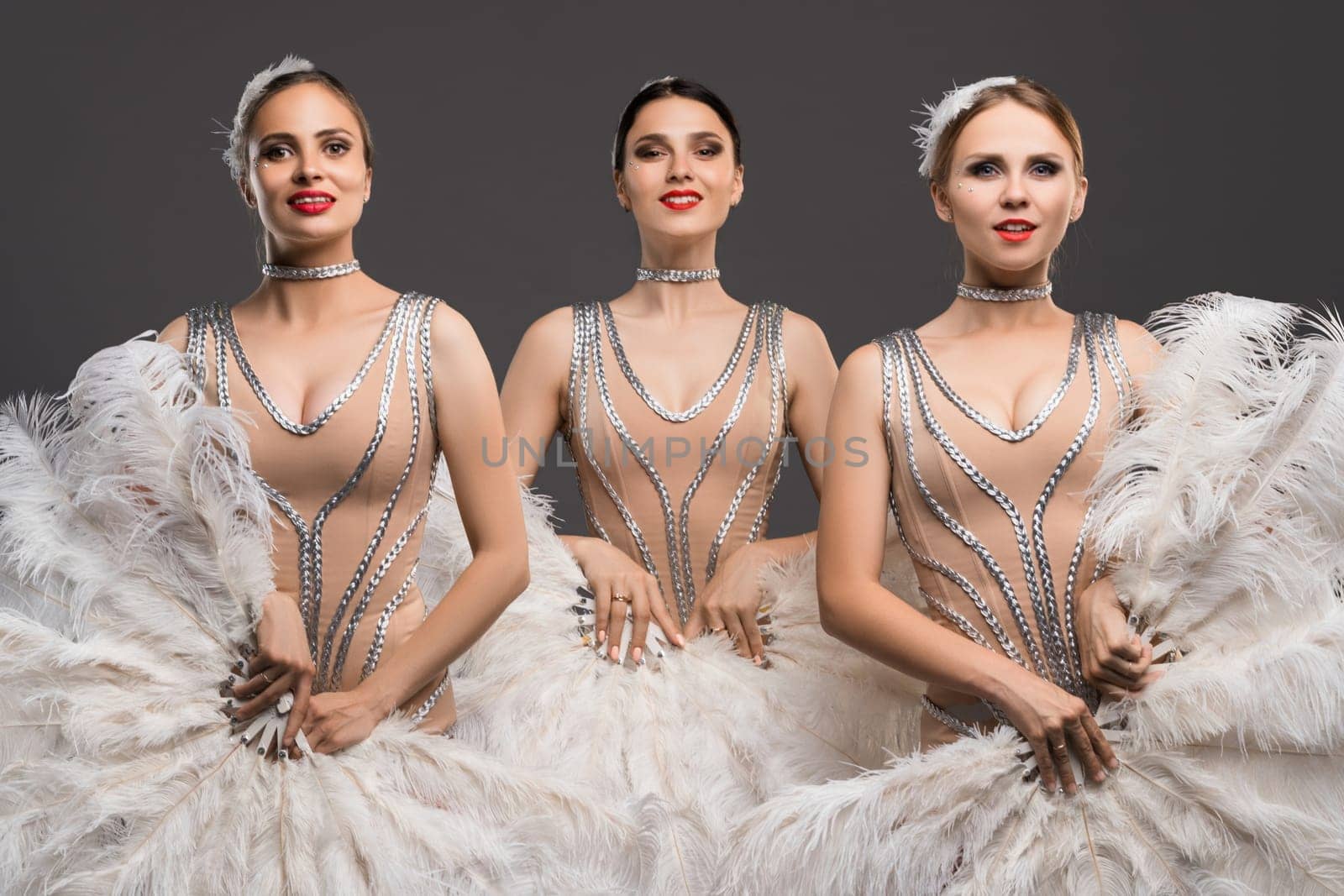 Three dancers in glamorous outfits display their beauty and skill while posing together, highlighting intricate designs and dynamic expressions.