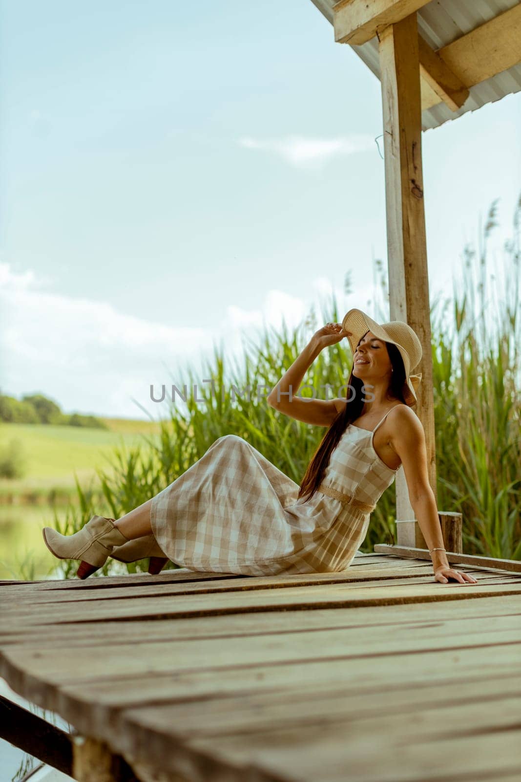 Young woman relaxing on the wooden pier at the calm lake on a hot summer day