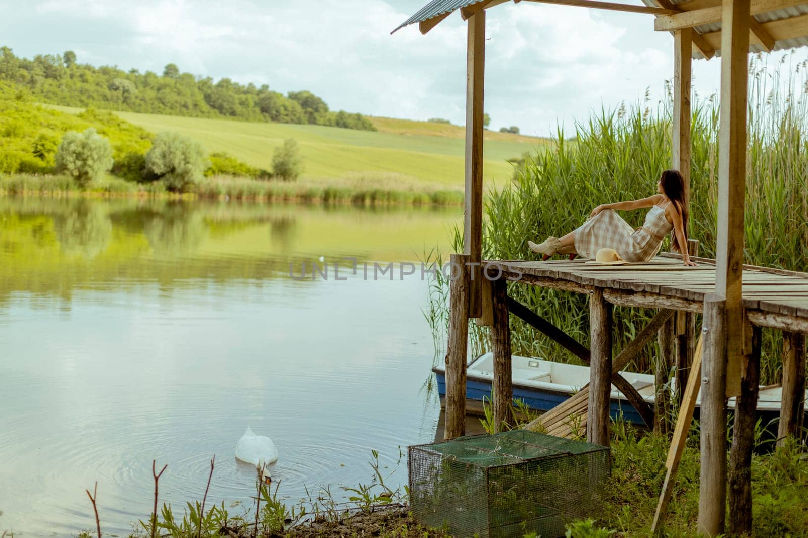 Young woman relaxing on the wooden pier at the calm lake on a hot summer day