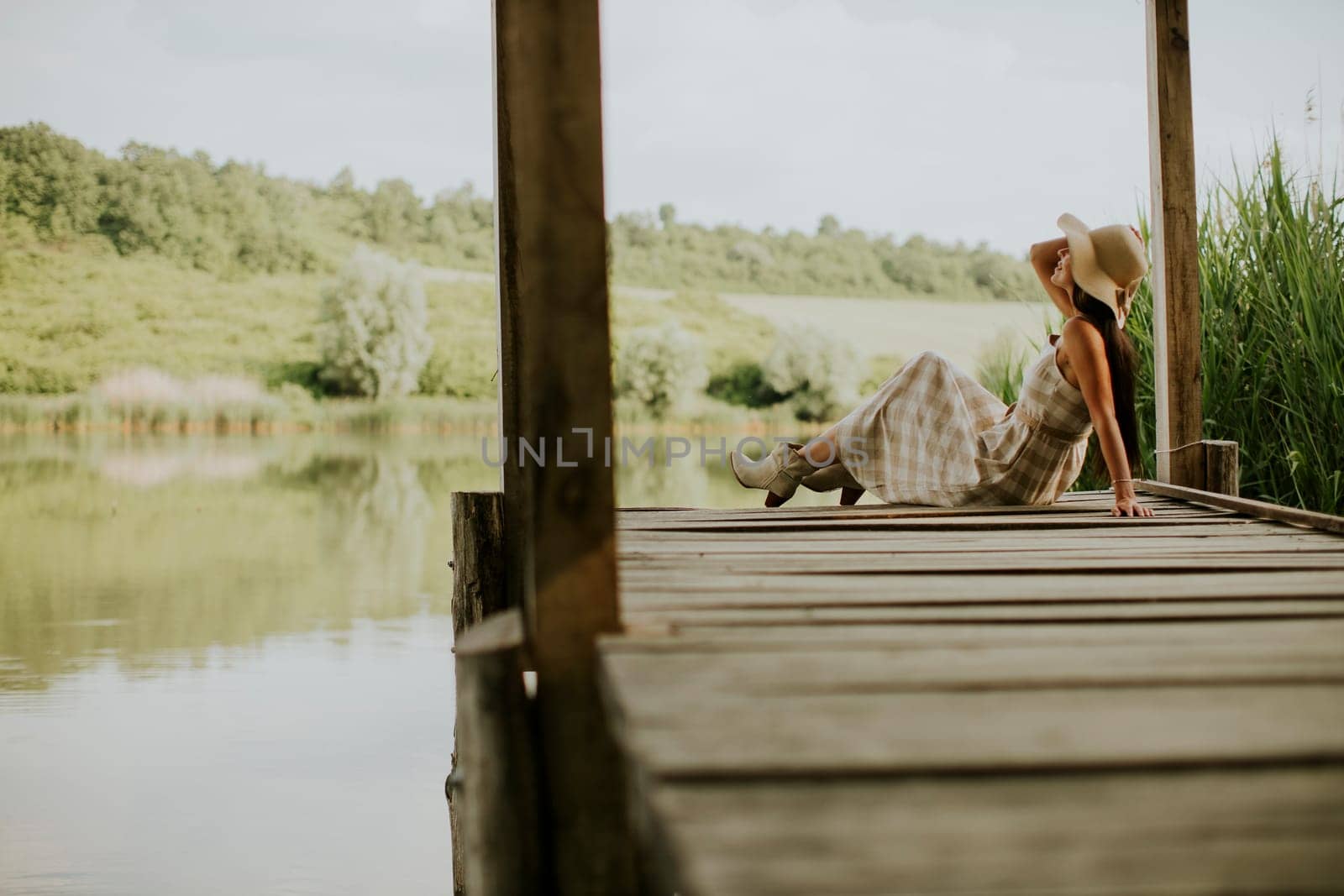 relaxing young woman on wooden pier at the calm lake
