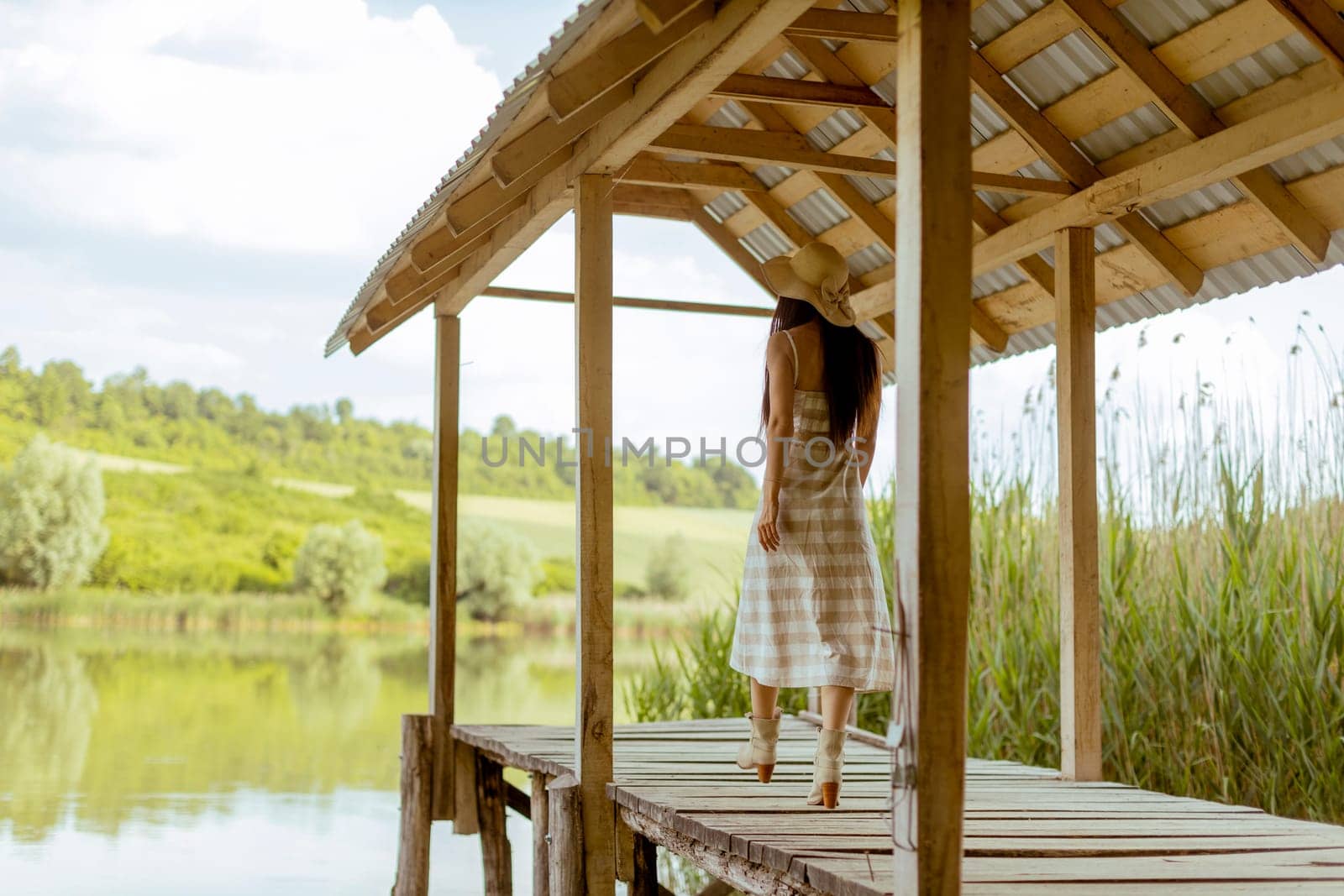 Young woman walking on the wooden pier at the calm lake on a hot summer day