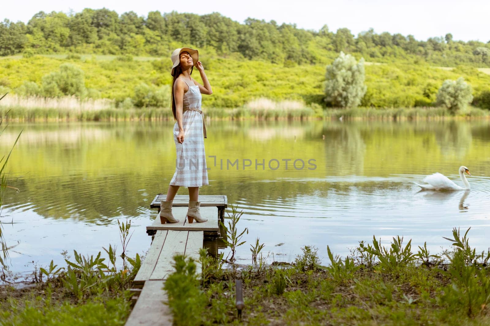 Young woman standing on the wooden pier at the calm lake on a hot summer day