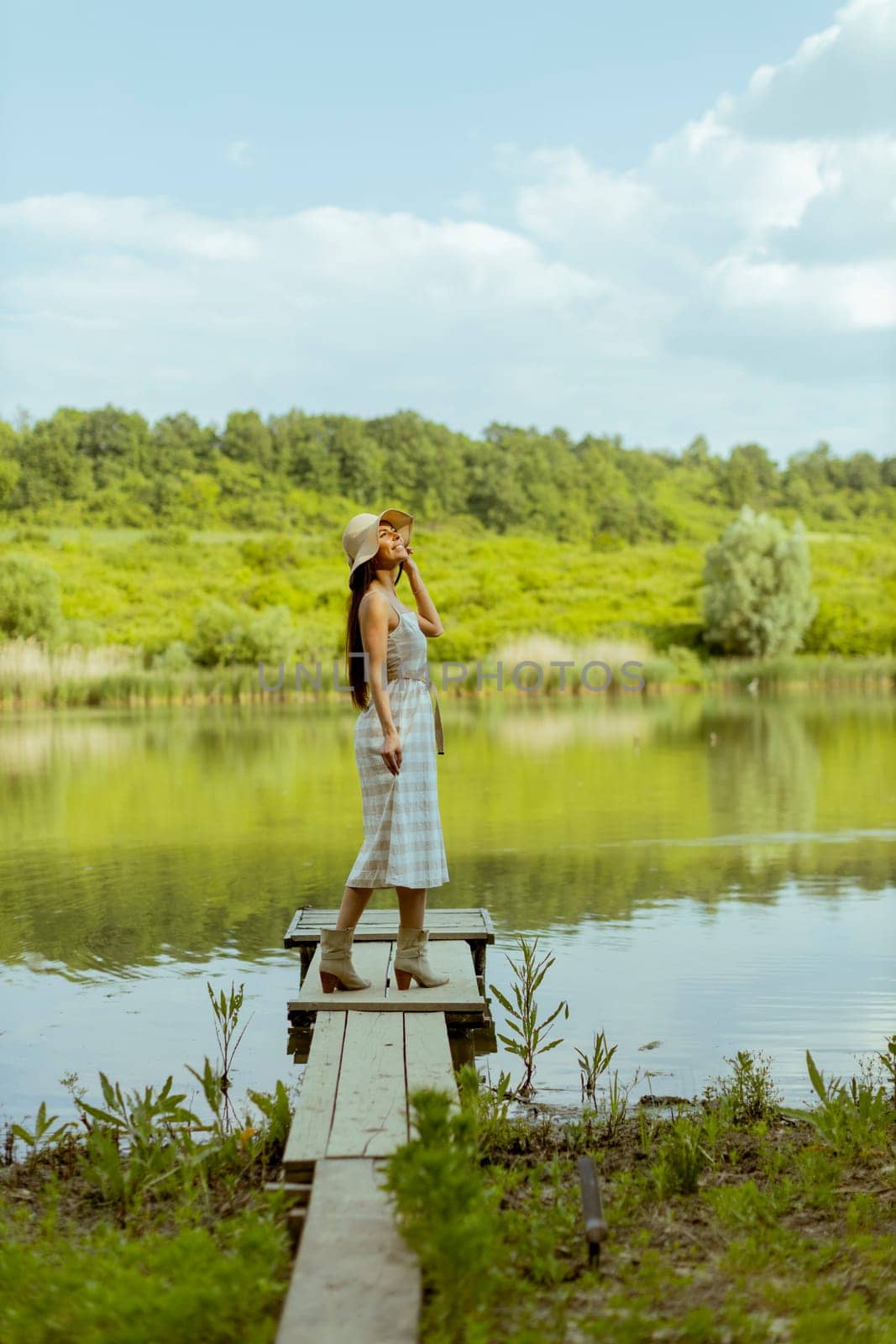 Young woman standing on the wooden pier at the calm lake on a hot summer day