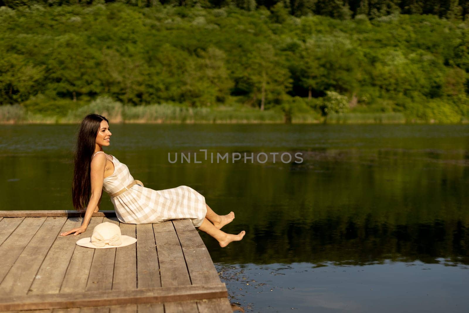 Young woman relaxing on the wooden pier at the calm lake on a hot summer day