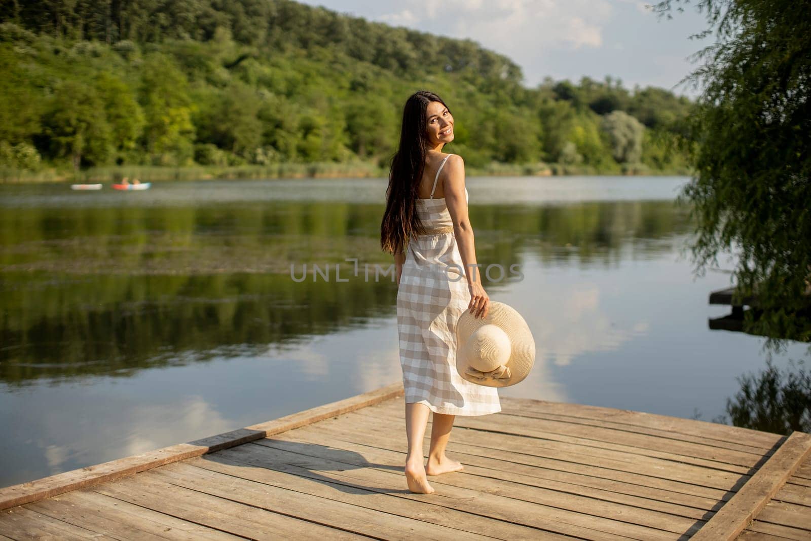 Relaxing young woman standing on wooden pier at the calm lake