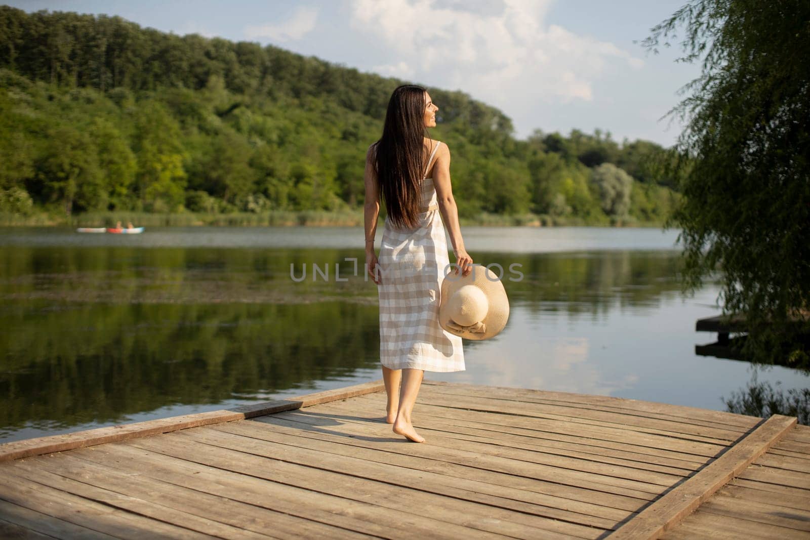 Relaxing young woman standing on wooden pier at the calm lake