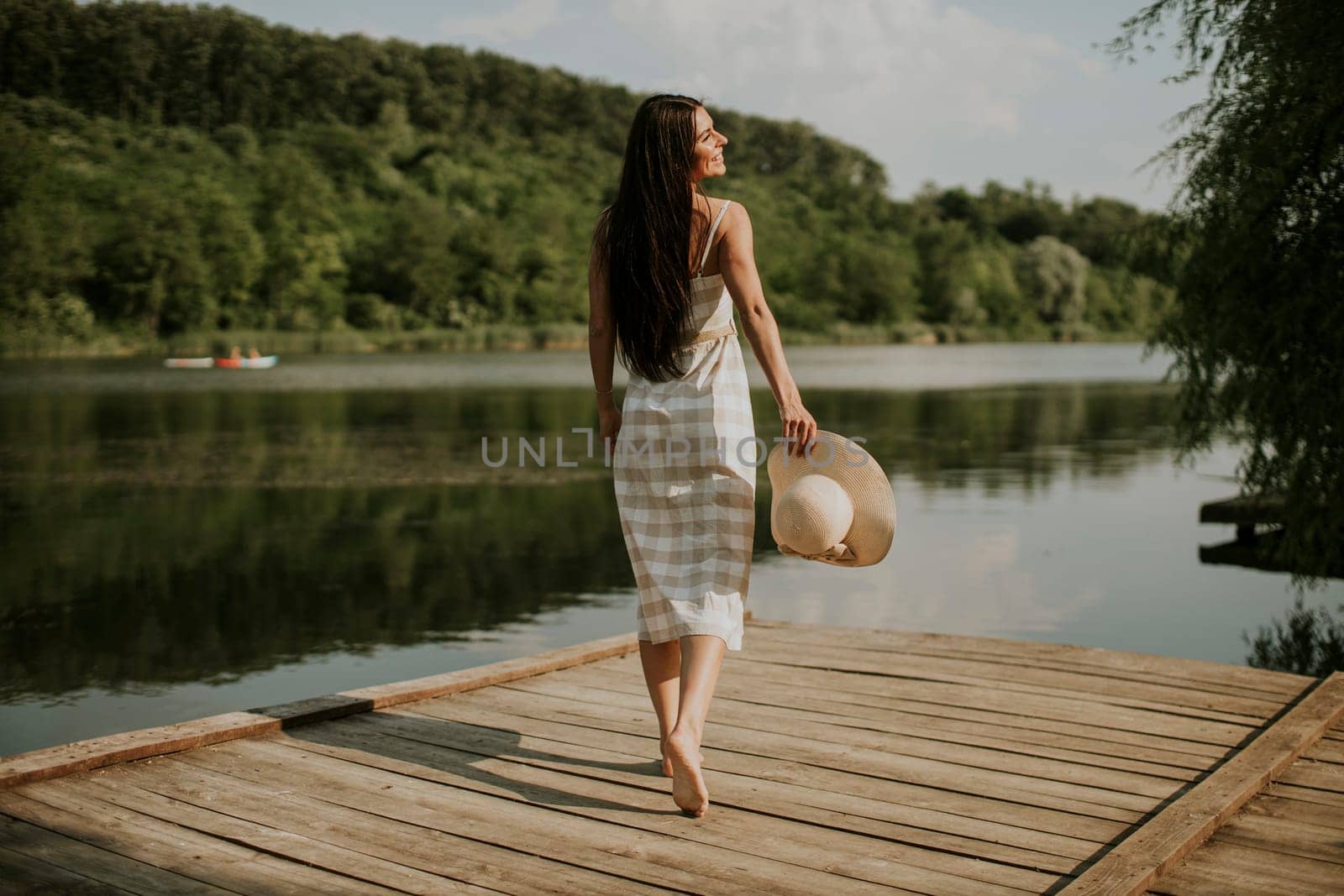 Relaxing young woman standing on wooden pier at the calm lake