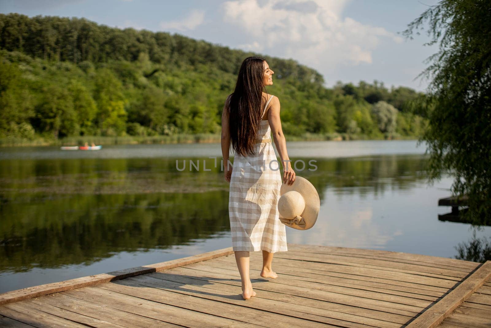 Relaxing young woman standing on wooden pier at the calm lake