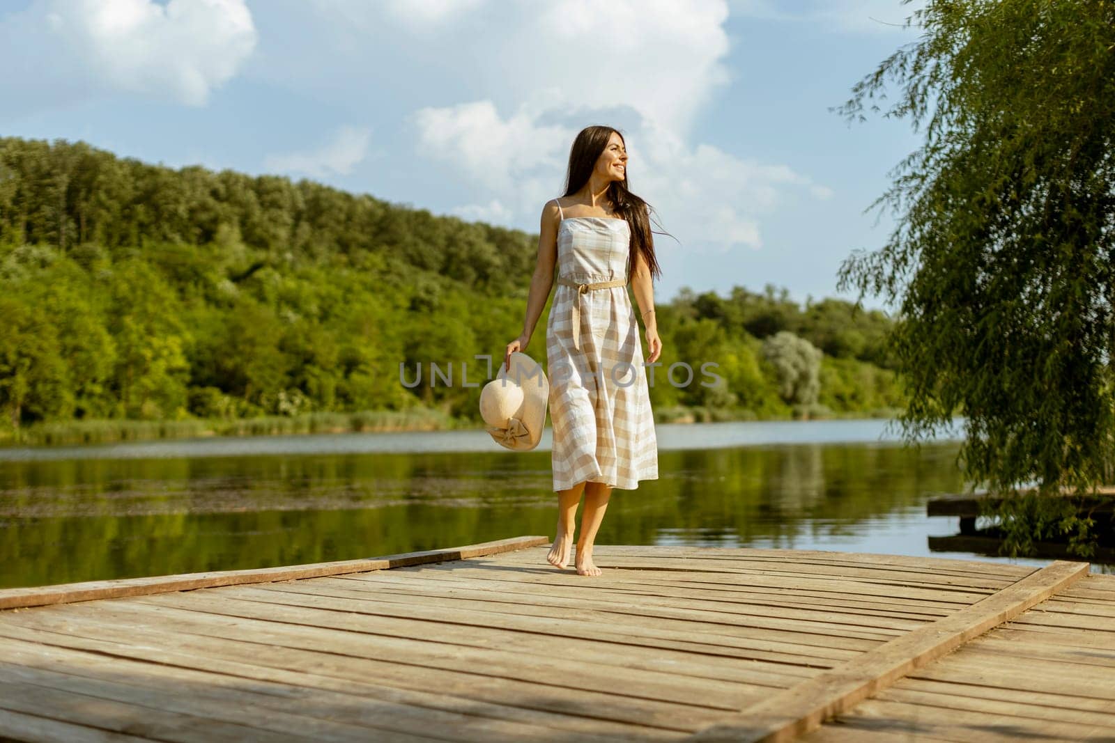 Young woman walking on the wooden pier at the calm lake on a hot summer day