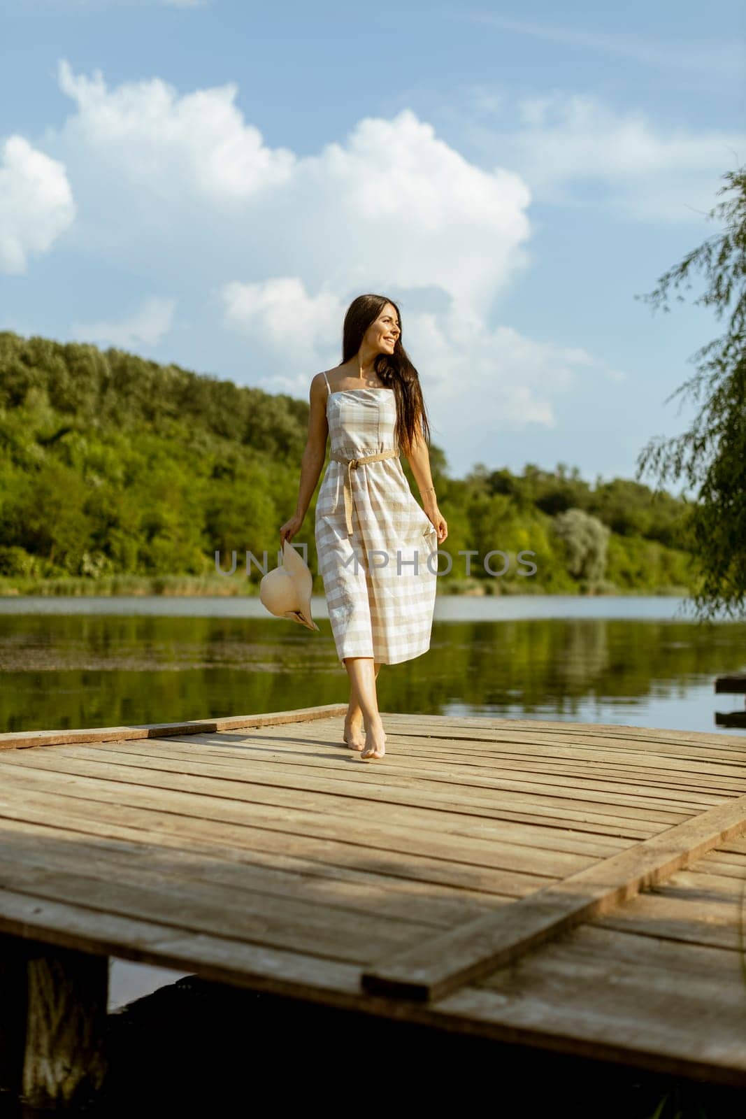 Young woman walking on the wooden pier at the calm lake on a hot summer day