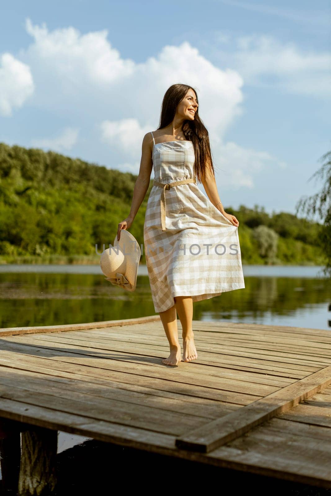 Young woman walking on the wooden pier at the calm lake on a hot summer day