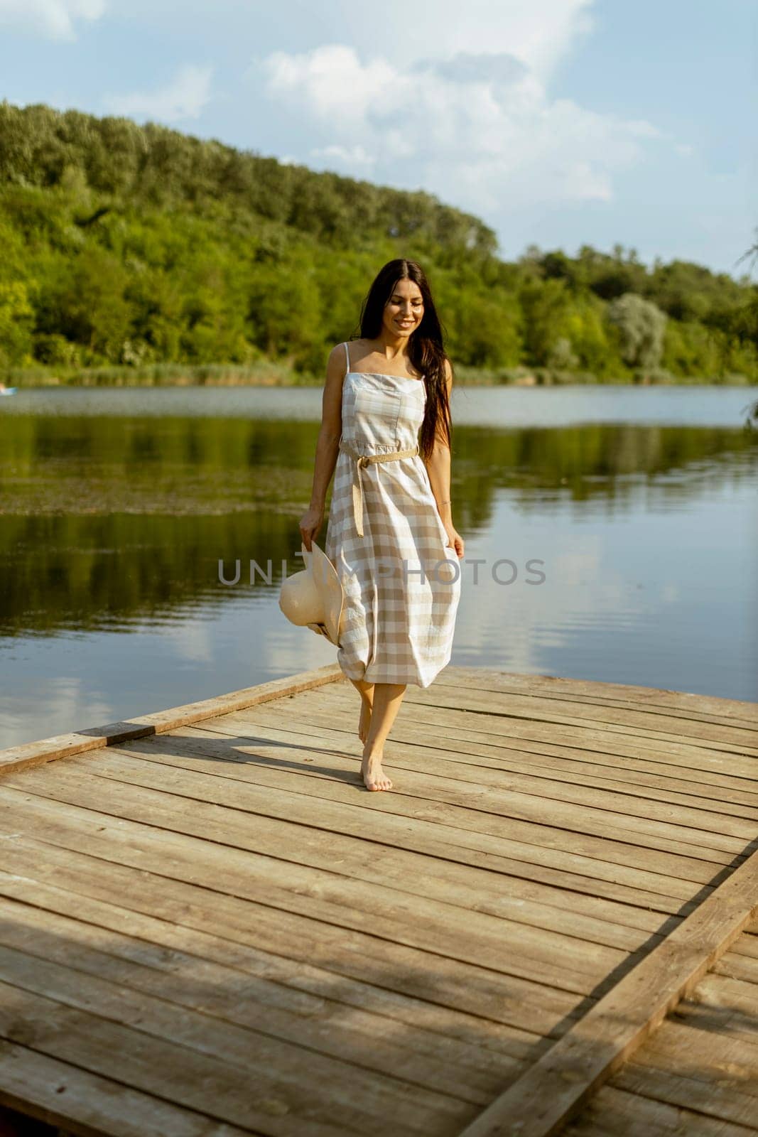 Young woman walking on the wooden pier at the calm lake on a hot summer day