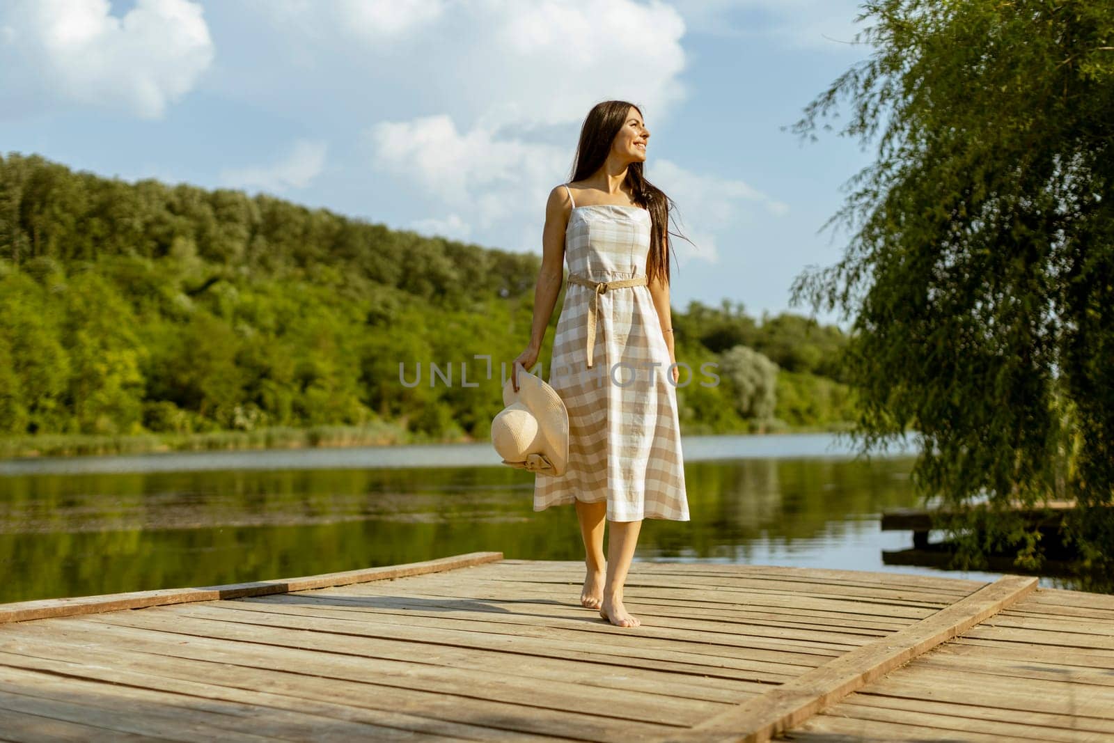 Young woman walking on the wooden pier at the calm lake on a hot summer day