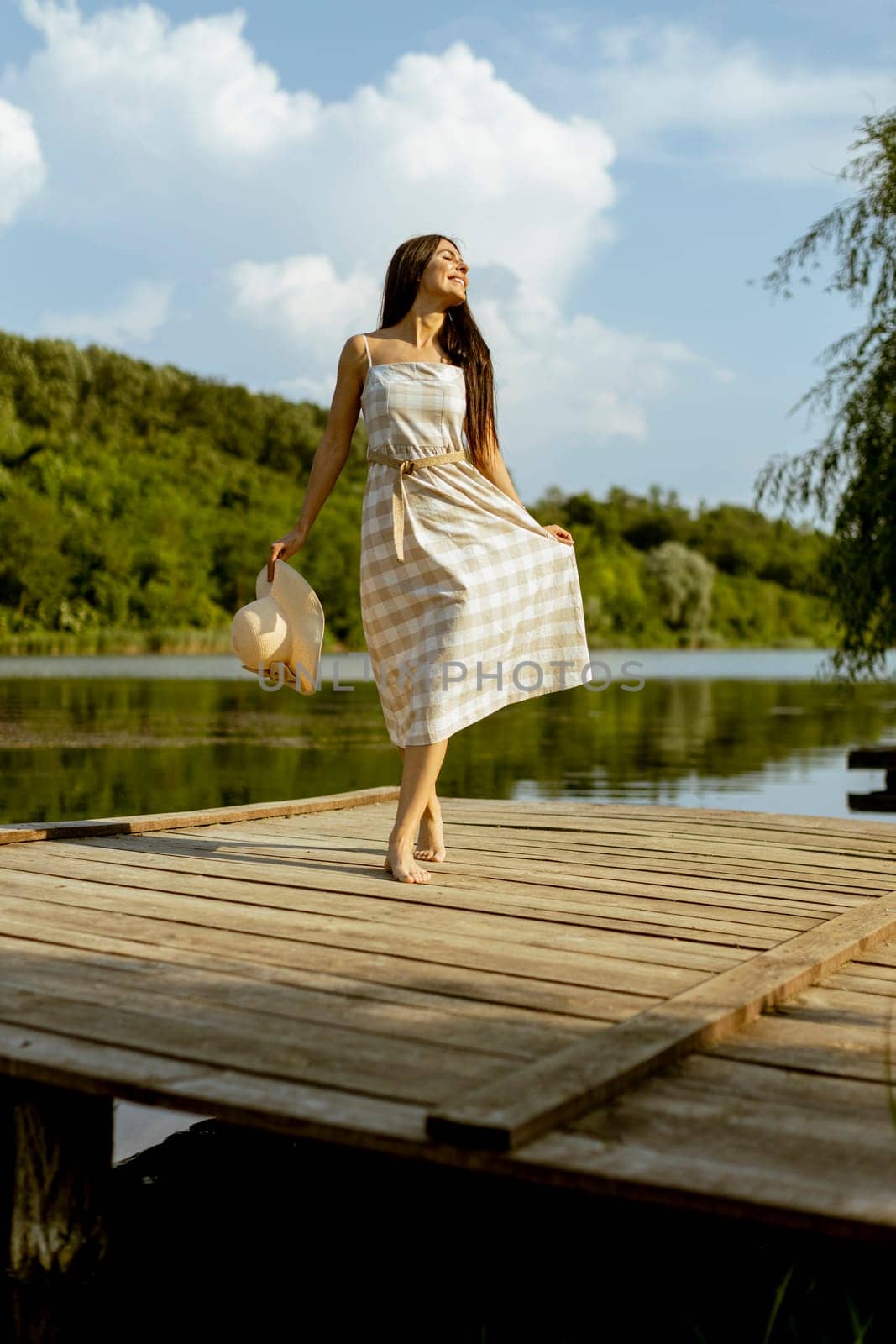 Young woman walking on the wooden pier at the calm lake on a hot summer day
