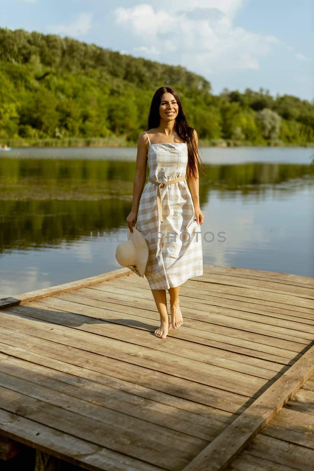 Young woman walking on the wooden pier at the calm lake on a hot summer day