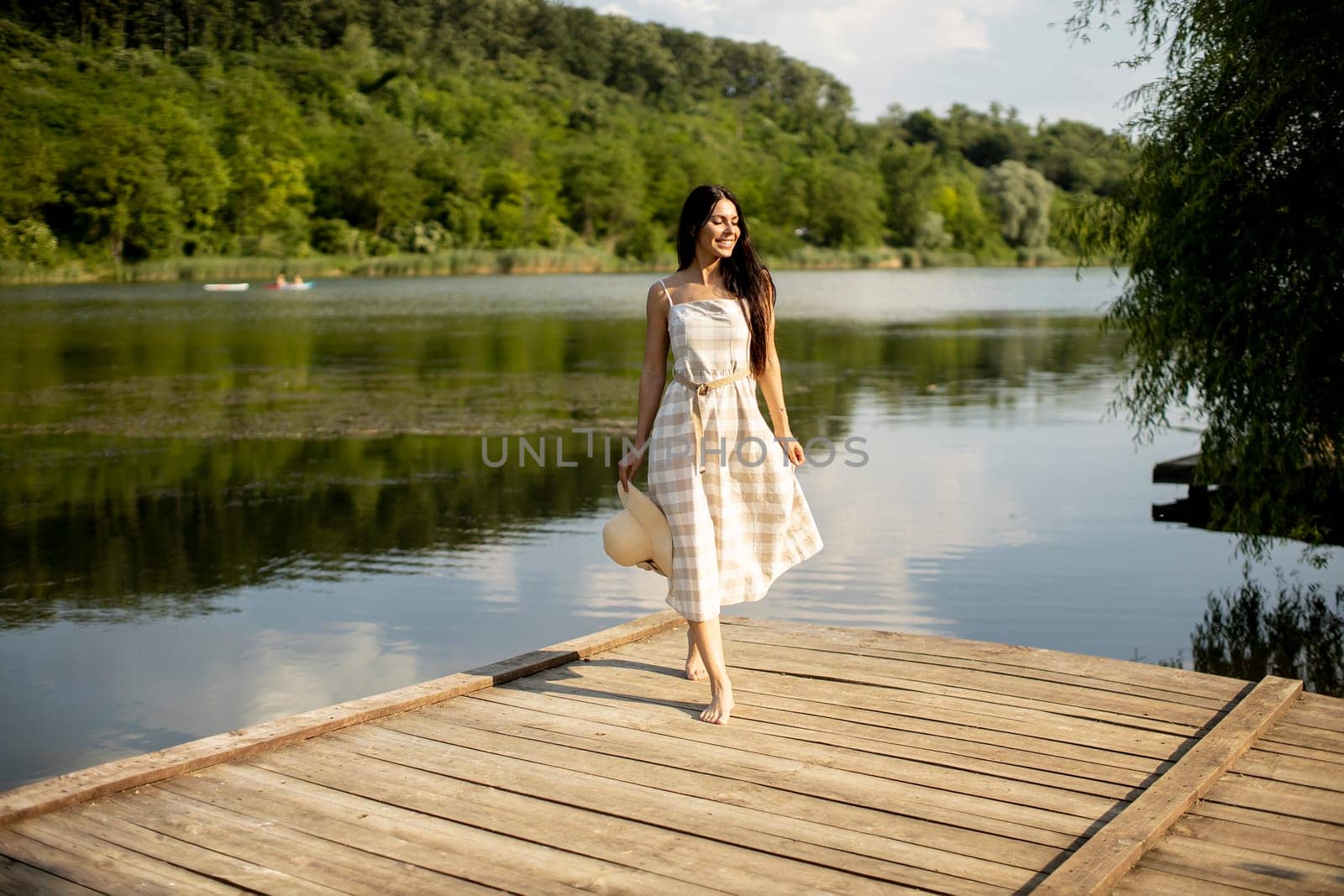 Relaxing young woman standing on wooden pier at the calm lake
