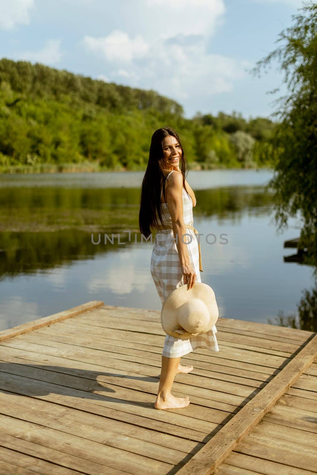 Young woman walking on the wooden pier at the calm lake on a hot summer day
