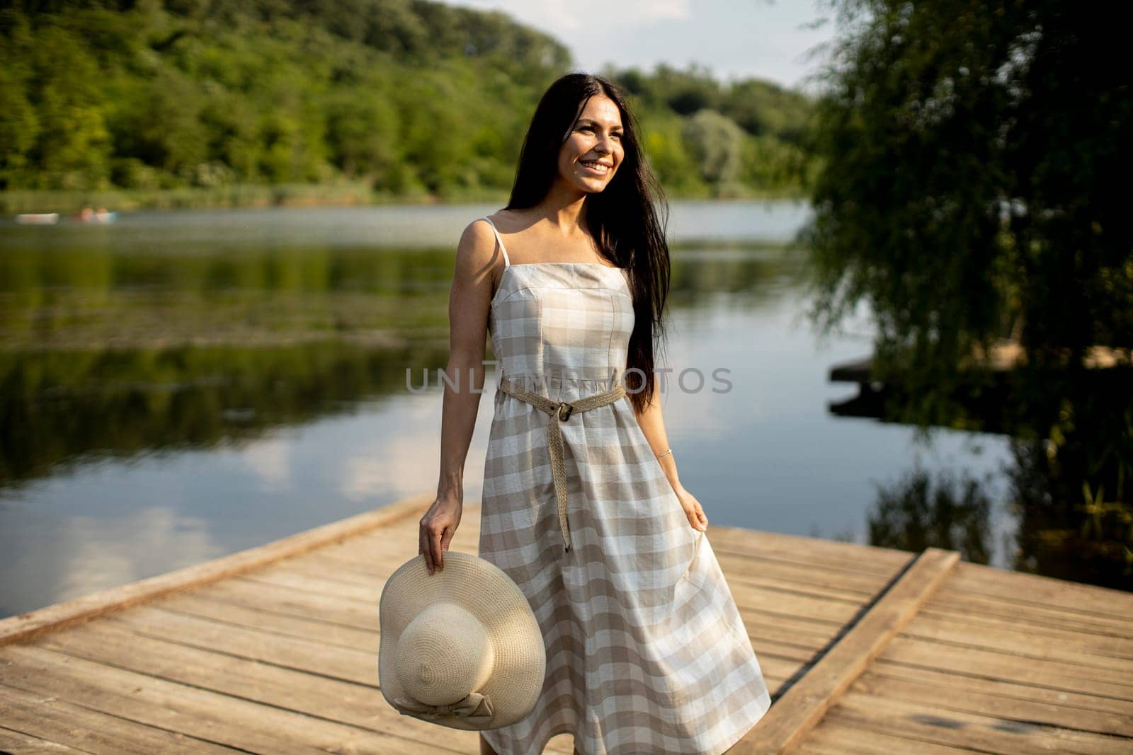 Relaxing young woman standing on wooden pier at the calm lake