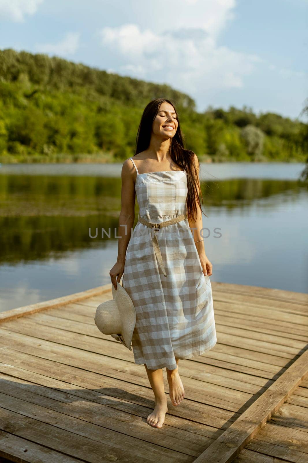 Young woman walking on the wooden pier at the calm lake on a hot summer day