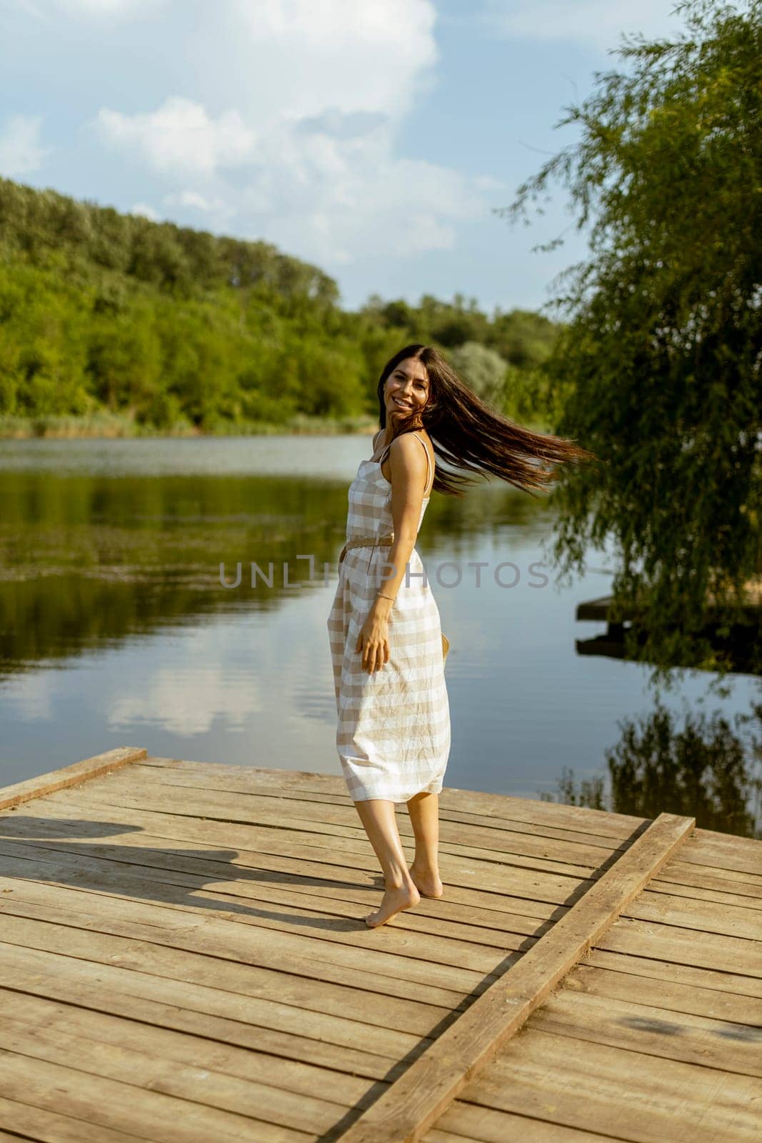 Young woman walking on the wooden pier at the calm lake on a hot summer day