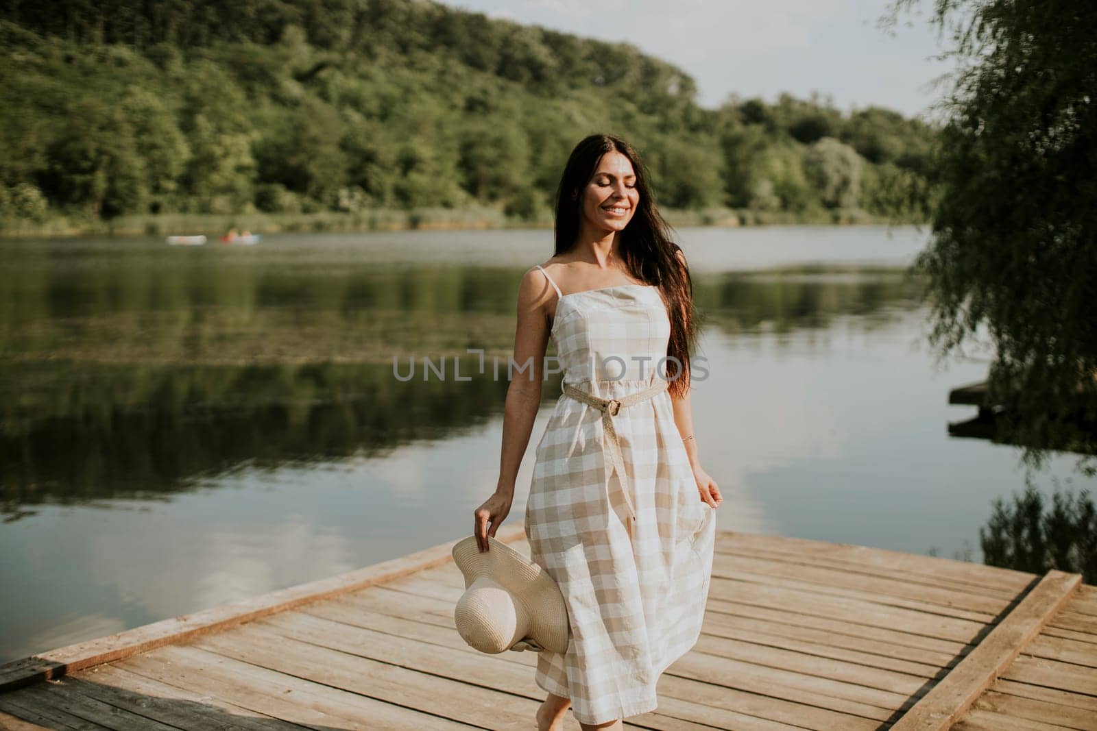 Relaxing young woman standing on wooden pier at the calm lake