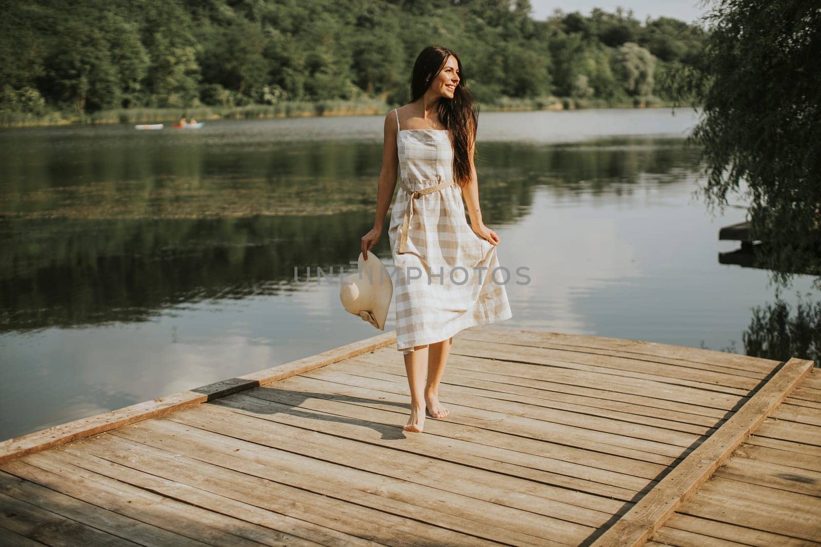Relaxing young woman standing on wooden pier at the calm lake