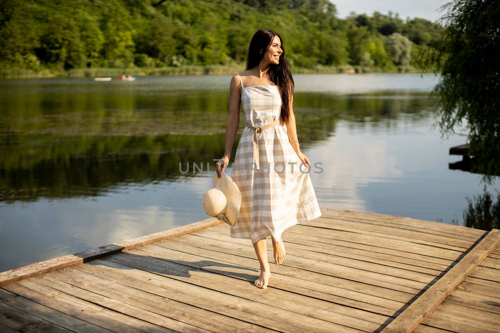 Relaxing young woman standing on wooden pier at the calm lake