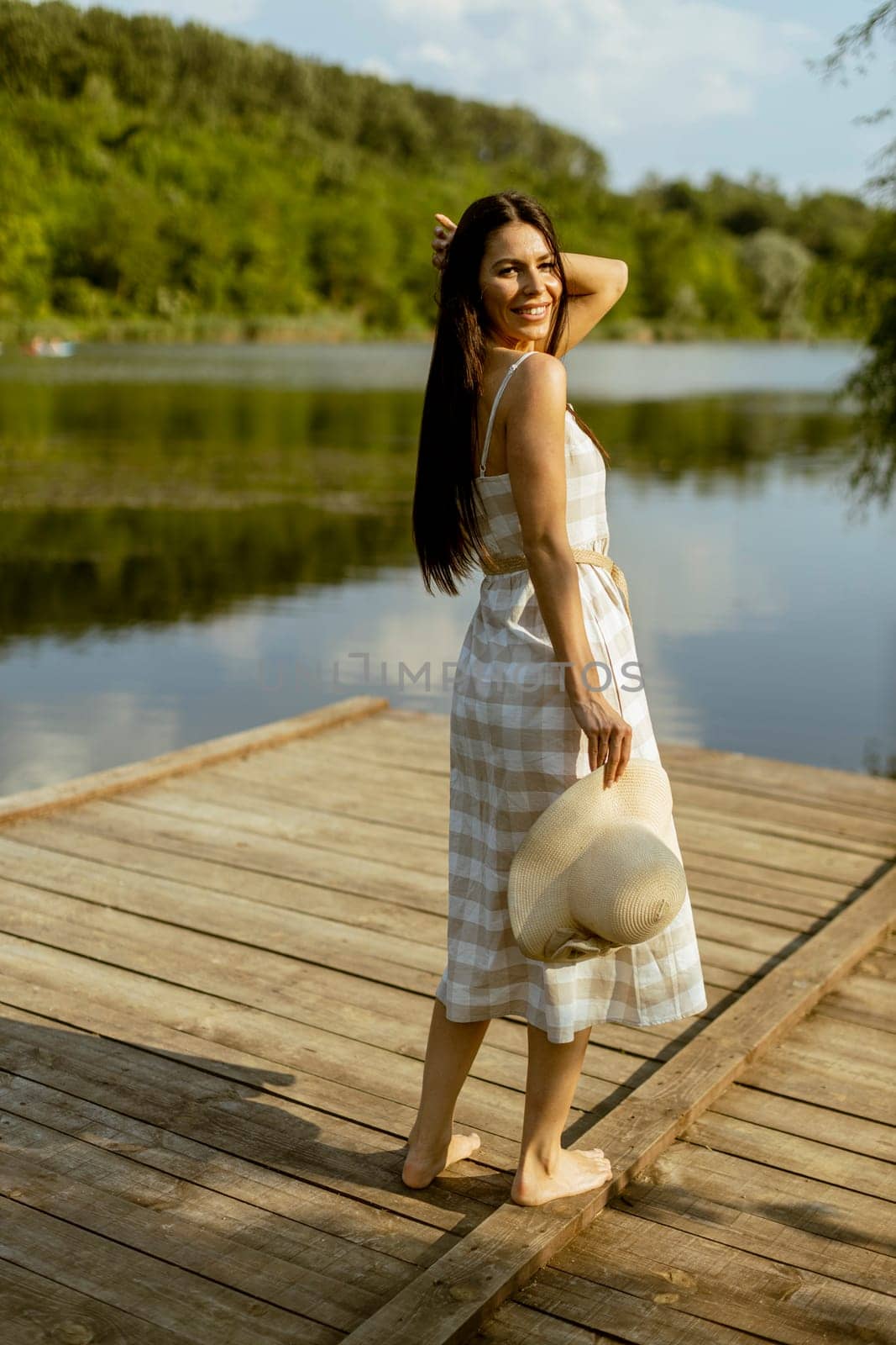 Young woman walking on the wooden pier at the calm lake on a hot summer day