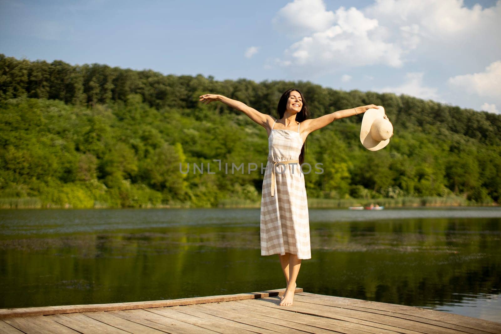 Relaxing young woman standing on wooden pier at the calm lake