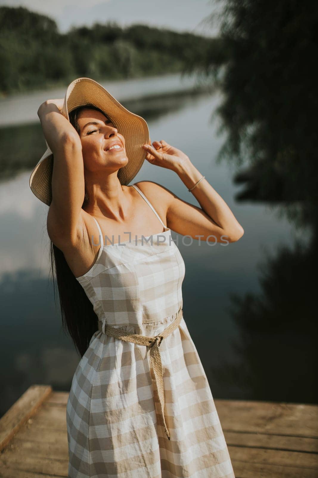 Relaxing young woman standing on wooden pier at the calm lake