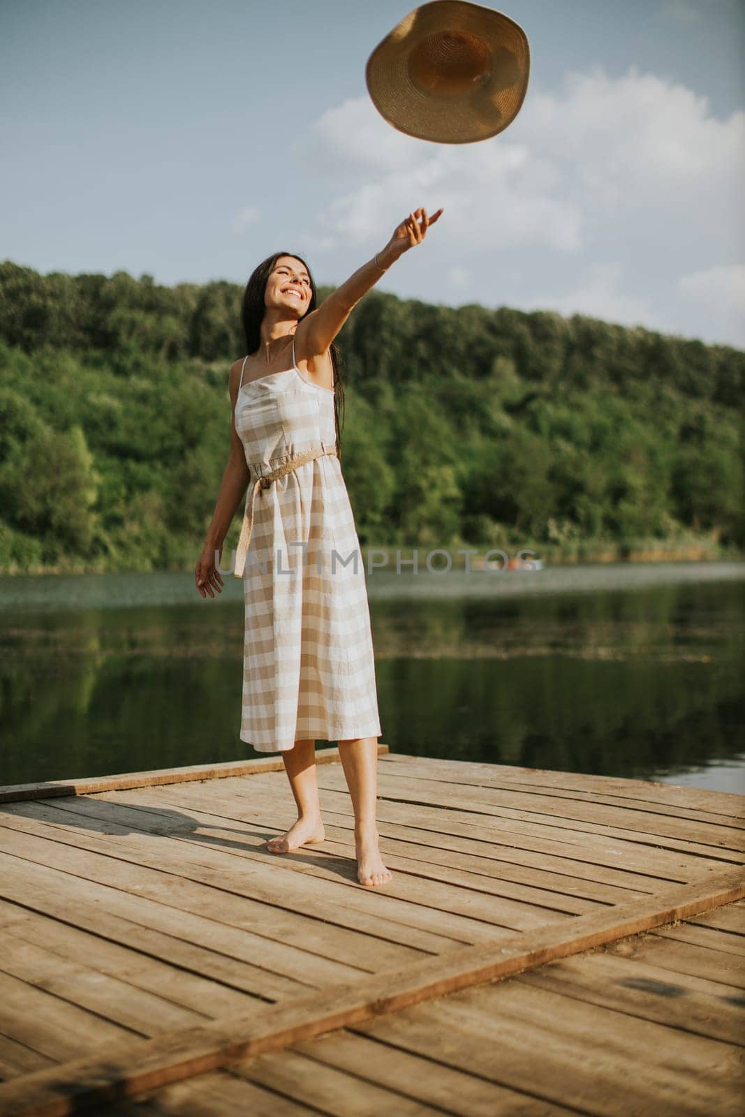 Happy young woman standing on wooden pier at the calm lake