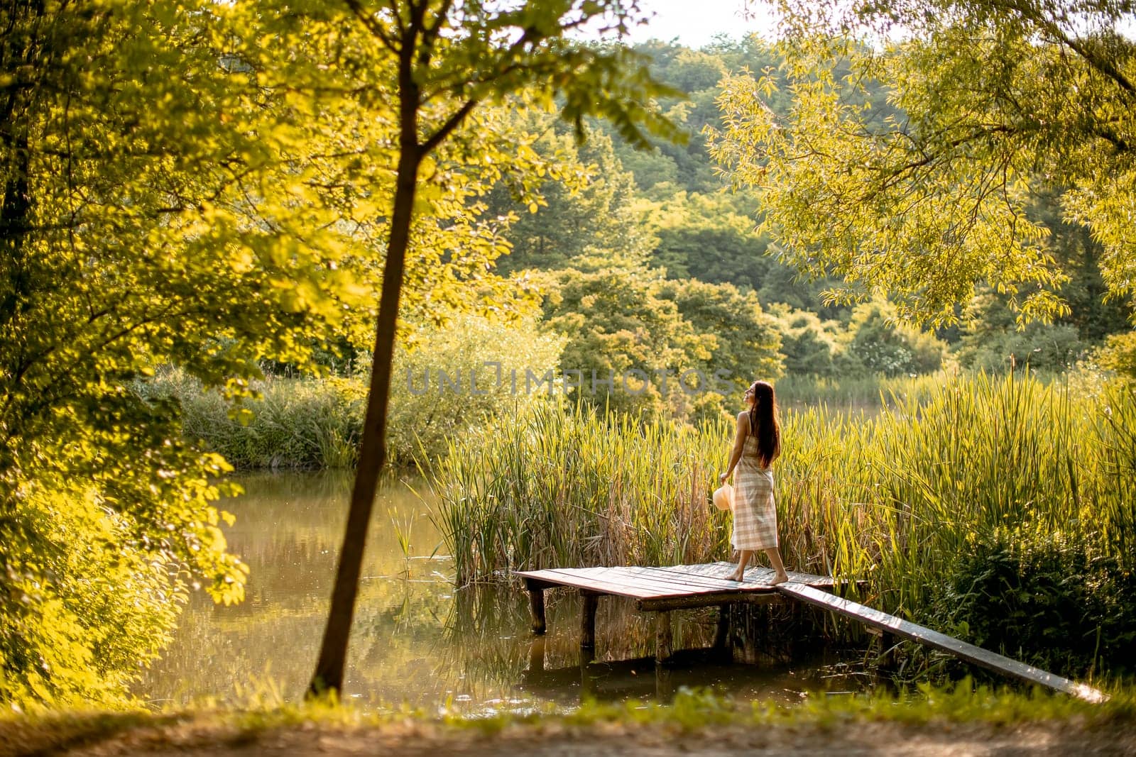 Young woman walking on the wooden pier at the calm lake on a hot summer day