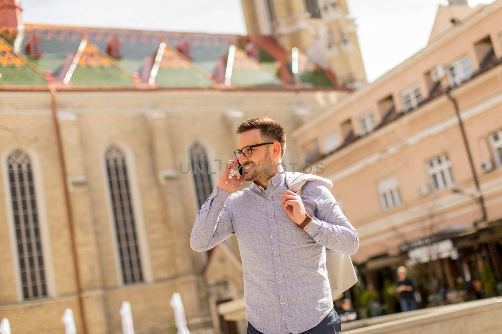 Cheerful young man uses mobile phone in urban enviroment at sunny day