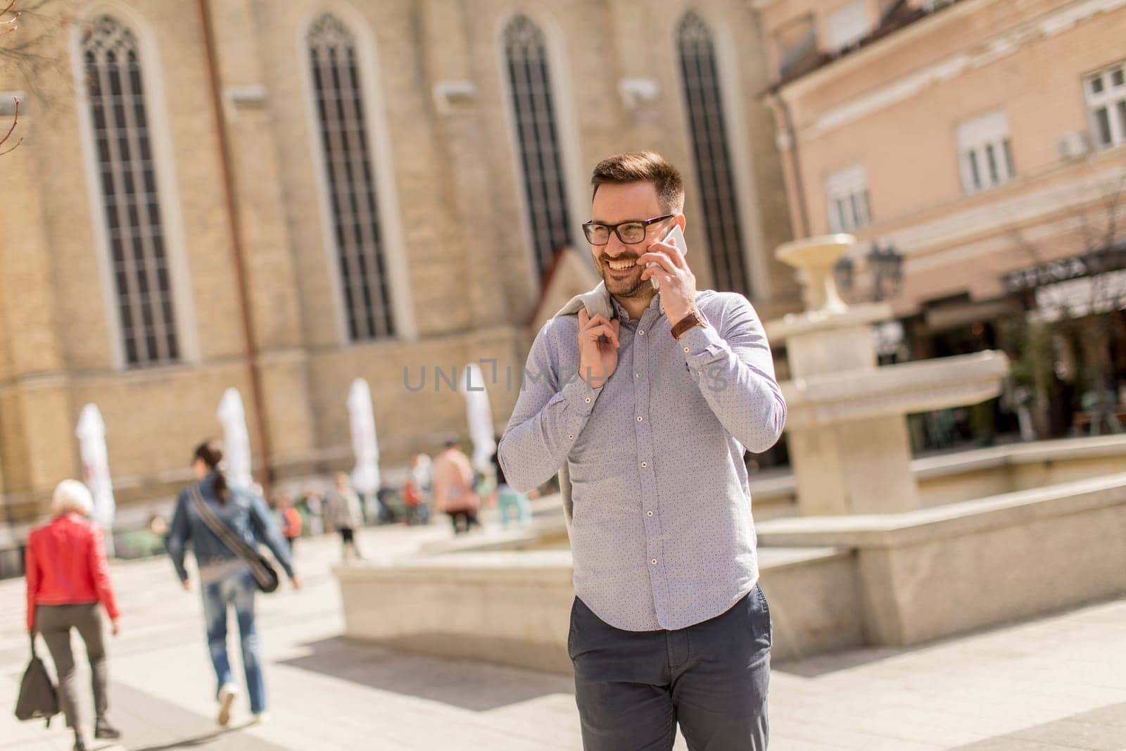 Cheerful young man uses mobile phone in urban enviroment at sunny day