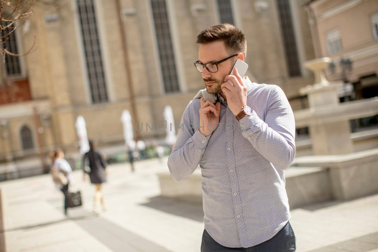Cheerful young man uses mobile phone in urban enviroment at sunny day