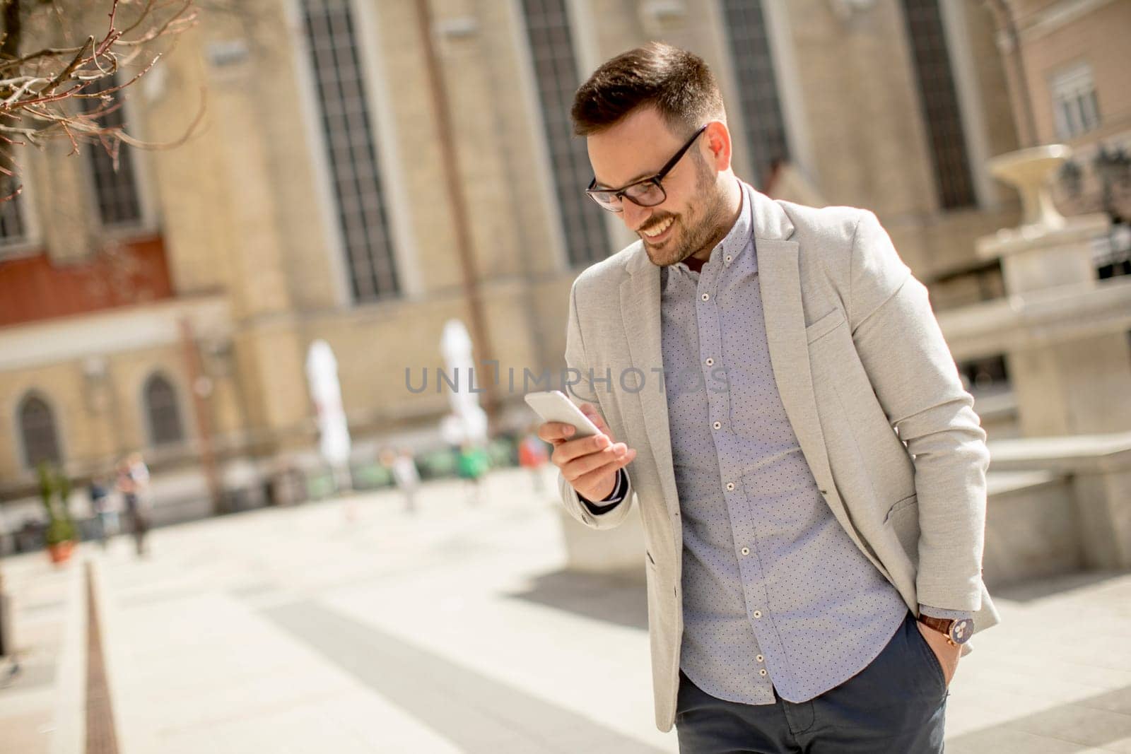 Cheerful young man uses mobile phone in urban enviroment at sunny day